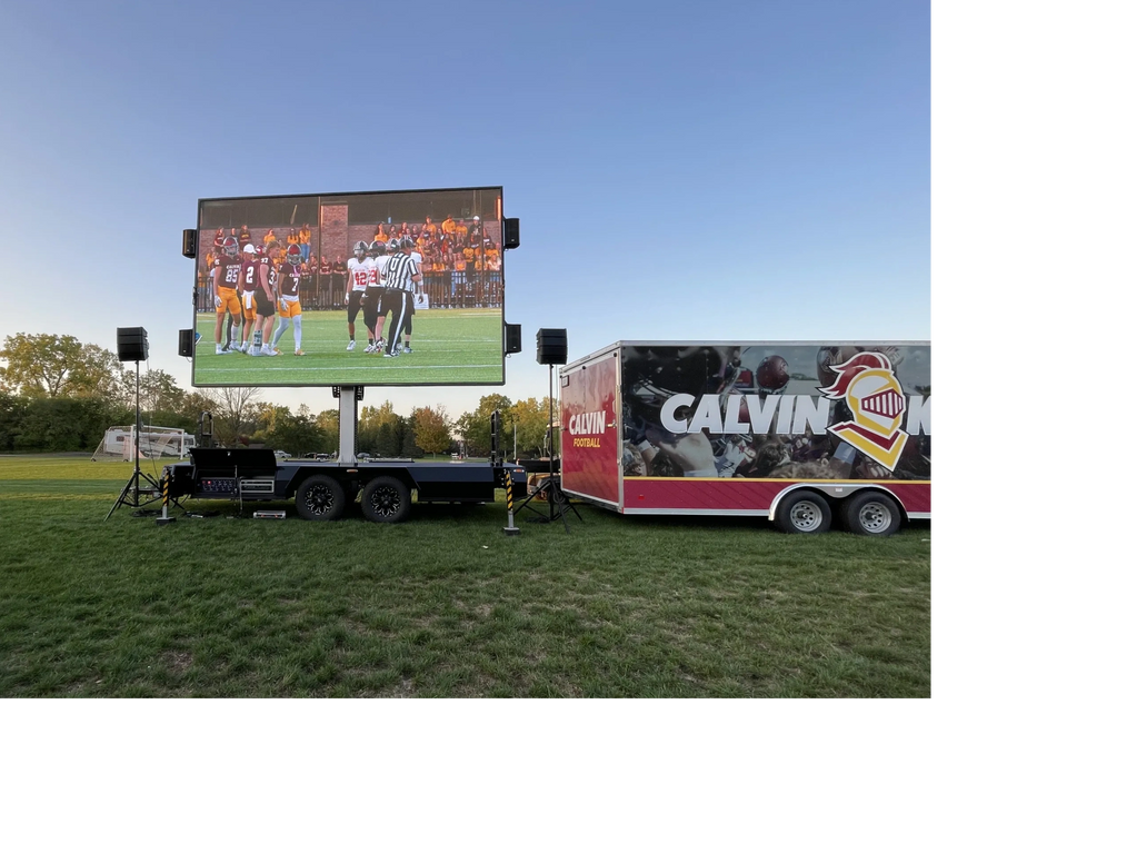 Outdoor screen showing a football game with Calvin Knights trailer nearby.
