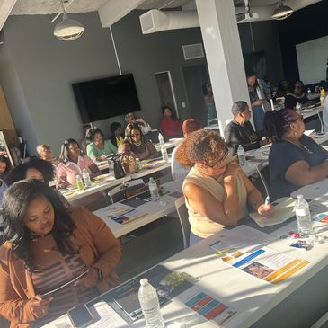 A group of people attentively participating in a daytime seminar or workshop indoors.