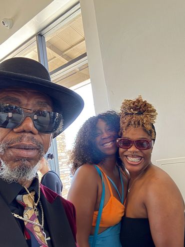 Three people smiling, one wearing a hat and glasses.