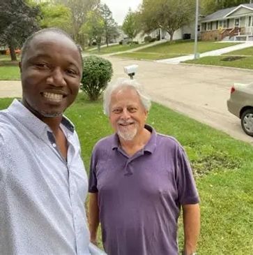 Two men smiling for a selfie in a suburban neighborhood.