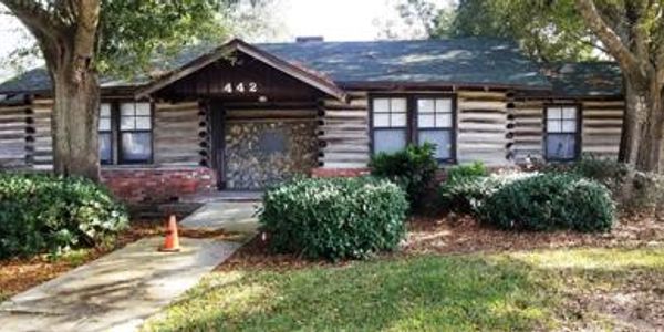 Front view of a rustic log cabin with a stone pathway and greenery.