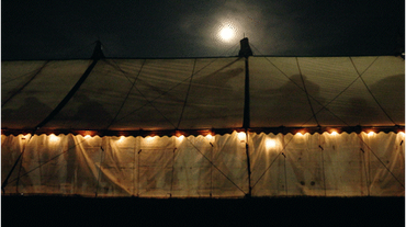 A dimly lit tent under a cloudy night sky with a glowing moon.