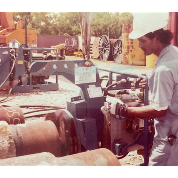 Worker operating machinery outdoors wearing a helmet and gloves.