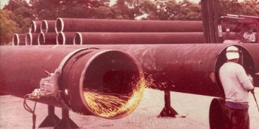 Worker cutting large metal pipe with sparks flying.