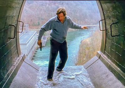A man holding a gun stands at the edge of a tunnel overlooking a river.