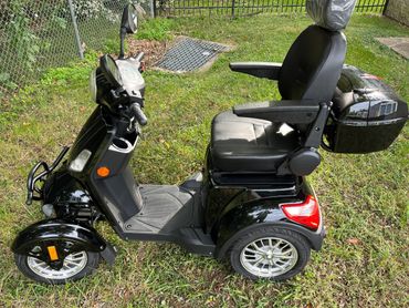 A black four-wheeled mobility scooter with a comfortable seat and armrests.