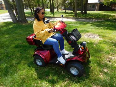 Woman riding a red mobility scooter on grass in a park.