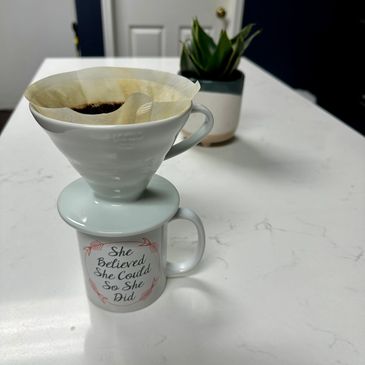 Coffee brewing setup with an inspirational mug on a white countertop.