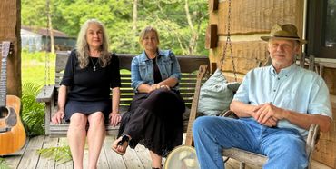 Ma Crow, Wendy Muncy, Dale Farmer sitting on front porch of log cabin