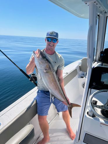 Man on boat proudly holding a large fish on a calm sea.