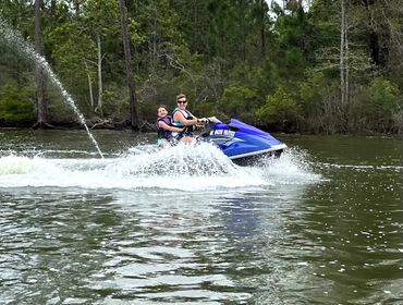 Two people riding a blue jet ski on a lake surrounded by trees.