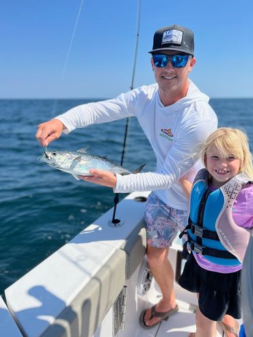 Man and child on boat showing a freshly caught fish on a sunny day.