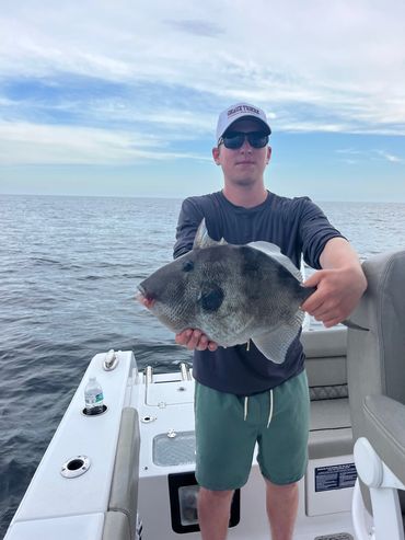 Man on boat holding a large fish with ocean in background.
