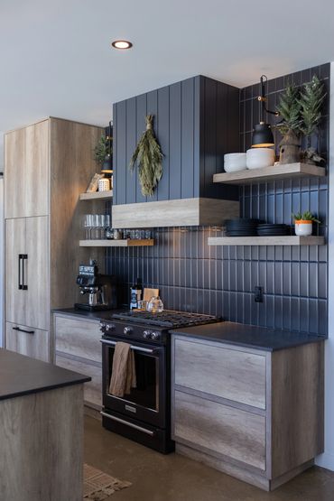 Close up of black stove and hood fan in kitchen with black backsplash and oak cabinets
