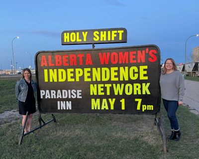 Two women stand beside a sign for Alberta Women's Independence Network event.