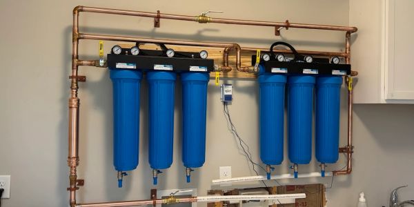 Industrial water filtration system with blue filter cartridges and gauges.