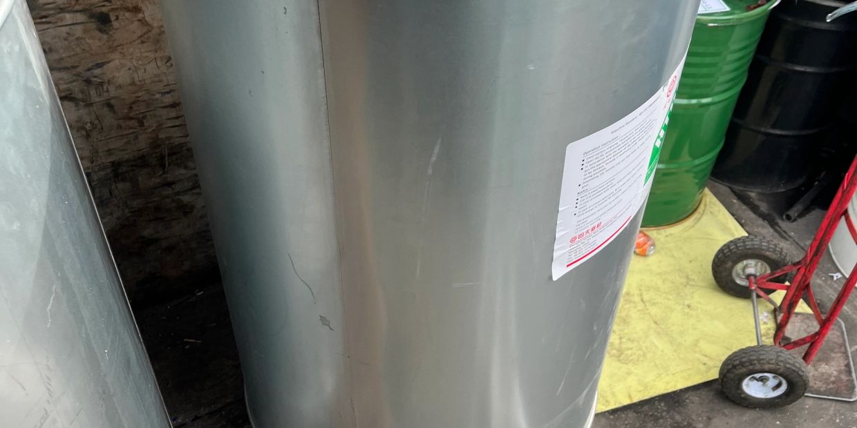 Large empty metal drum with label on a workshop floor.