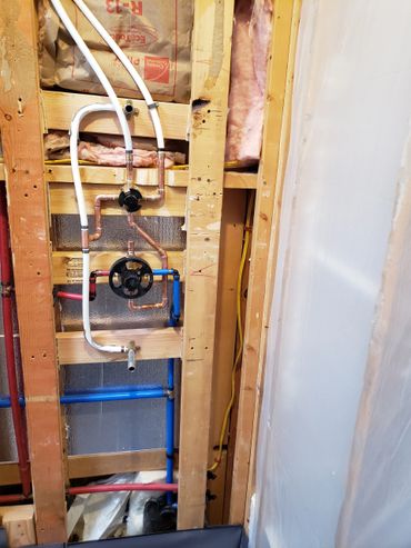 Exposed plumbing and insulation inside a wooden frame wall under construction.
