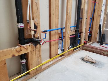 Exposed plumbing and piping in a building under construction with a measuring tape extended.