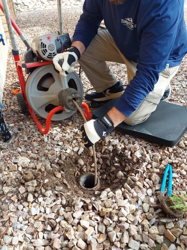 Plumber using a drain snake to clear a clogged pipe outdoors.