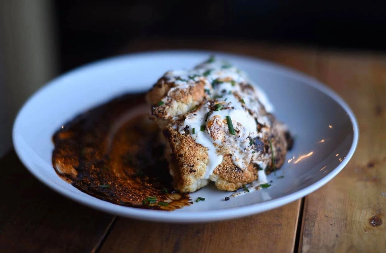 Roasted cauliflower with creamy sauce and herbs on a white plate.
