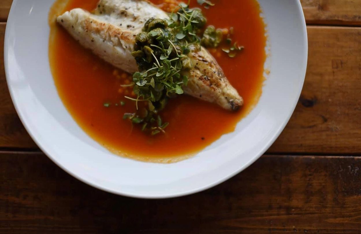 Grilled fish fillet with green garnish in a red sauce on a white plate.