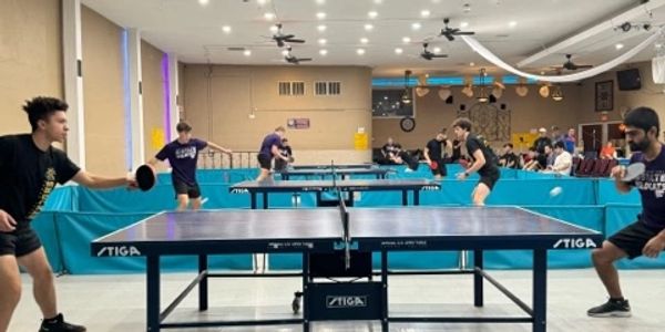 Young players engaged in a competitive table tennis match in an indoor sports hall.