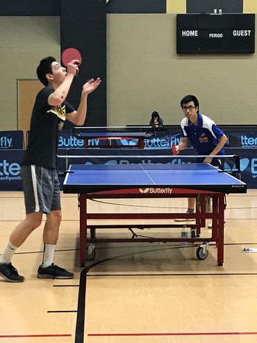 Two men playing table tennis indoors on a Butterfly table.