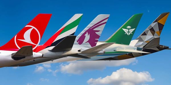 Five airplane tails with distinct airline logos against a clear blue sky.