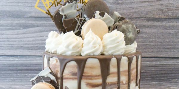 Chocolate drip cake with macarons and whipped cream decoration.