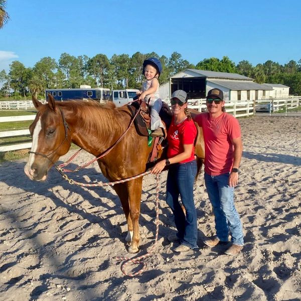 Happy child riding a horse with two adults beside them in a sunny farm setting.