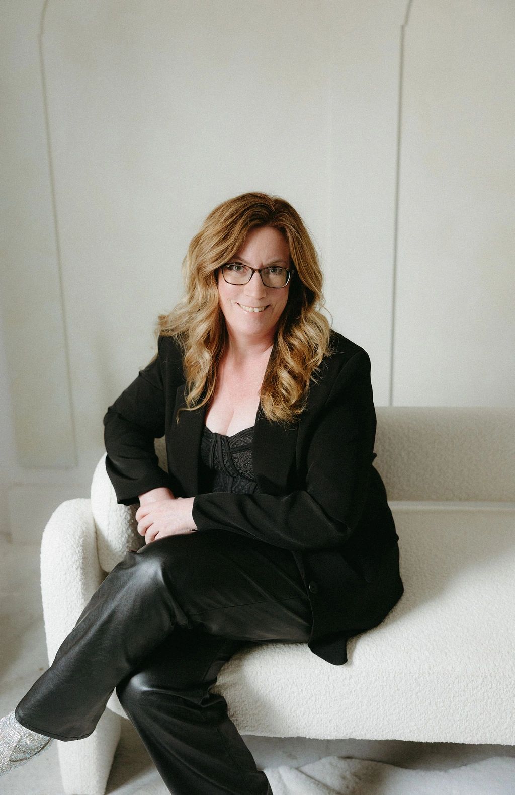 Woman in black attire sitting on a white couch, smiling.