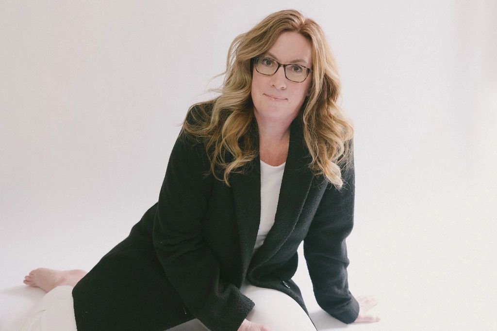 Woman with glasses wearing black coat and white pants.