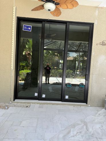 Newly installed black-framed sliding glass door with reflections of greenery and a person taking a photo.