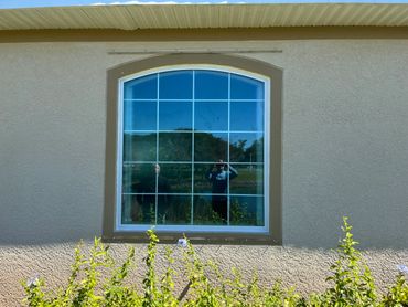 Two people reflected in a large window with garden plants in front.