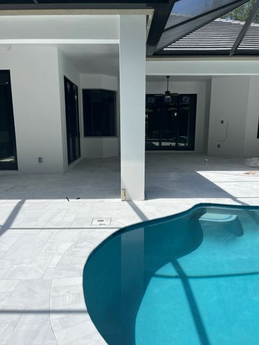 Modern backyard with a clean pool and white tiled patio under a screened enclosure.