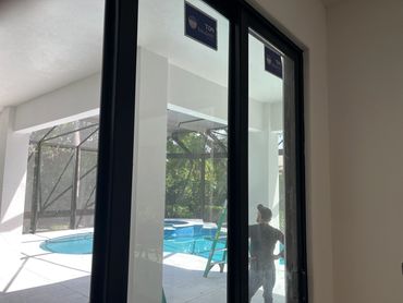 Man standing by a pool near a ladder, viewed through glass doors.