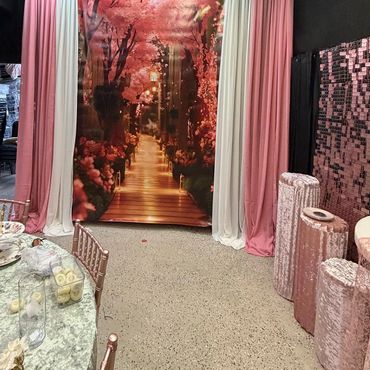 Elegant event setup with pink and white drapes and a floral pathway backdrop.
