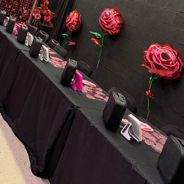 Long table with black covers, rose balloons, and makeup kits.