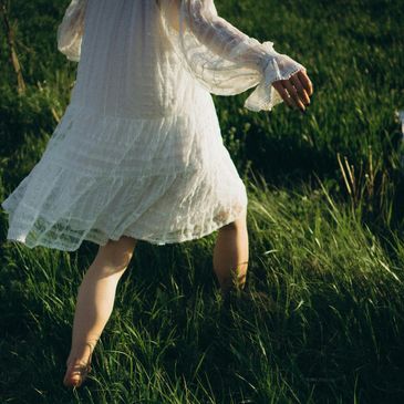 Person in a white dress walking barefoot in grass.