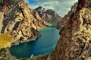 A stunning turquoise lake surrounded by rugged rocky mountains under a partly cloudy sky.
