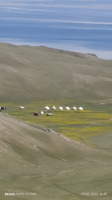 A remote settlement with yurts in a vast mountainous landscape under a clear blue sky.