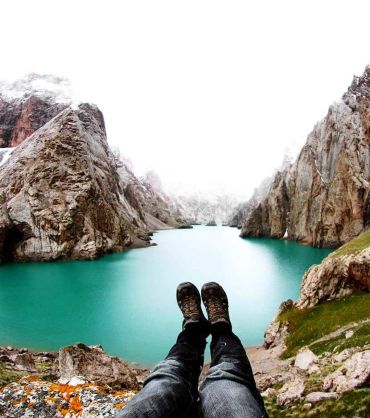 Person relaxing with feet up overlooking a turquoise mountain lake.
