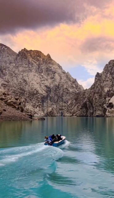 A group of people boating on a tranquil lake surrounded by rocky mountains at sunset.