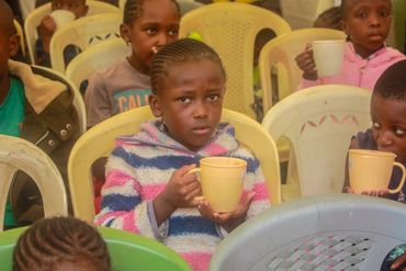 January 20th Action - young children in chairs drinking porridge from yellow cups
