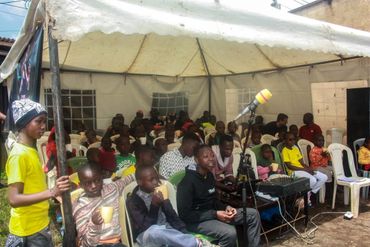 January 20th Action - Children in chairs under a tent drinking from yellow mugs of porridge