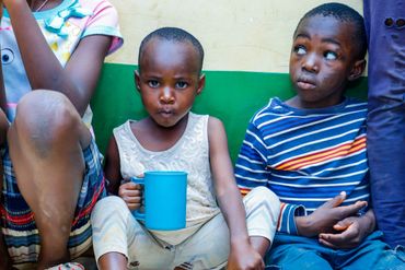 February 10th Action - Children sitting along a wall, one child with a blue mug of porridge