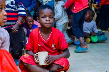 February 10th Action - Young boy in red holding a white mug of porridge