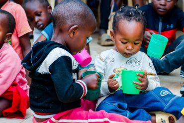 February 10th Action - Children sitting on the floor with cups of porridge in their hands