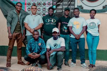 February 10th Action - Group of eight adults posing together in front of a sign for undugu